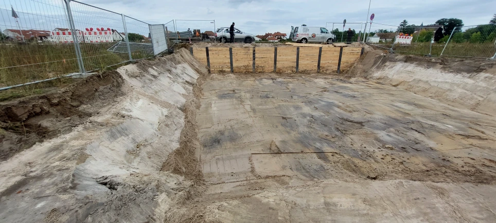 Excavation with timber boards between steel beams and adjacent sloped soil faces