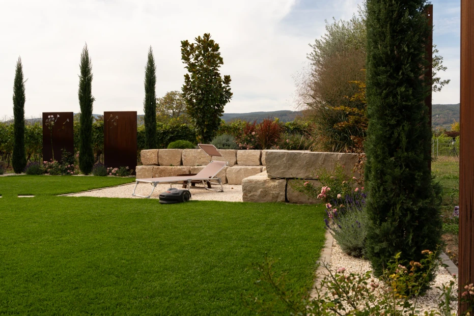 Wide lawn with slender woody plants and an enclosed seating area in the background