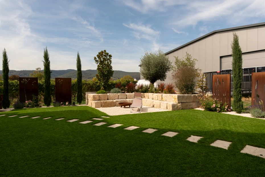 Garden in Niederkirchen with stepping stones in the lawn and a gravel area enclosed by natural stone walls