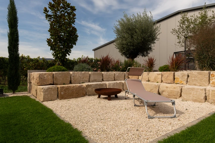 Light gravel area with a garden lounger, fire bowl and an enclosure of large natural stone blocks