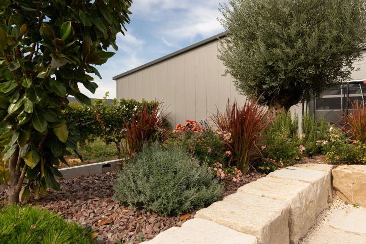 Light natural stone wall in front of a garden bed with woody plants, grasses and flowering plants