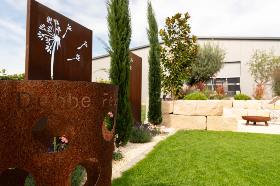 Rust-coloured garden decorations and privacy screens in front of woody plants and natural stone edging