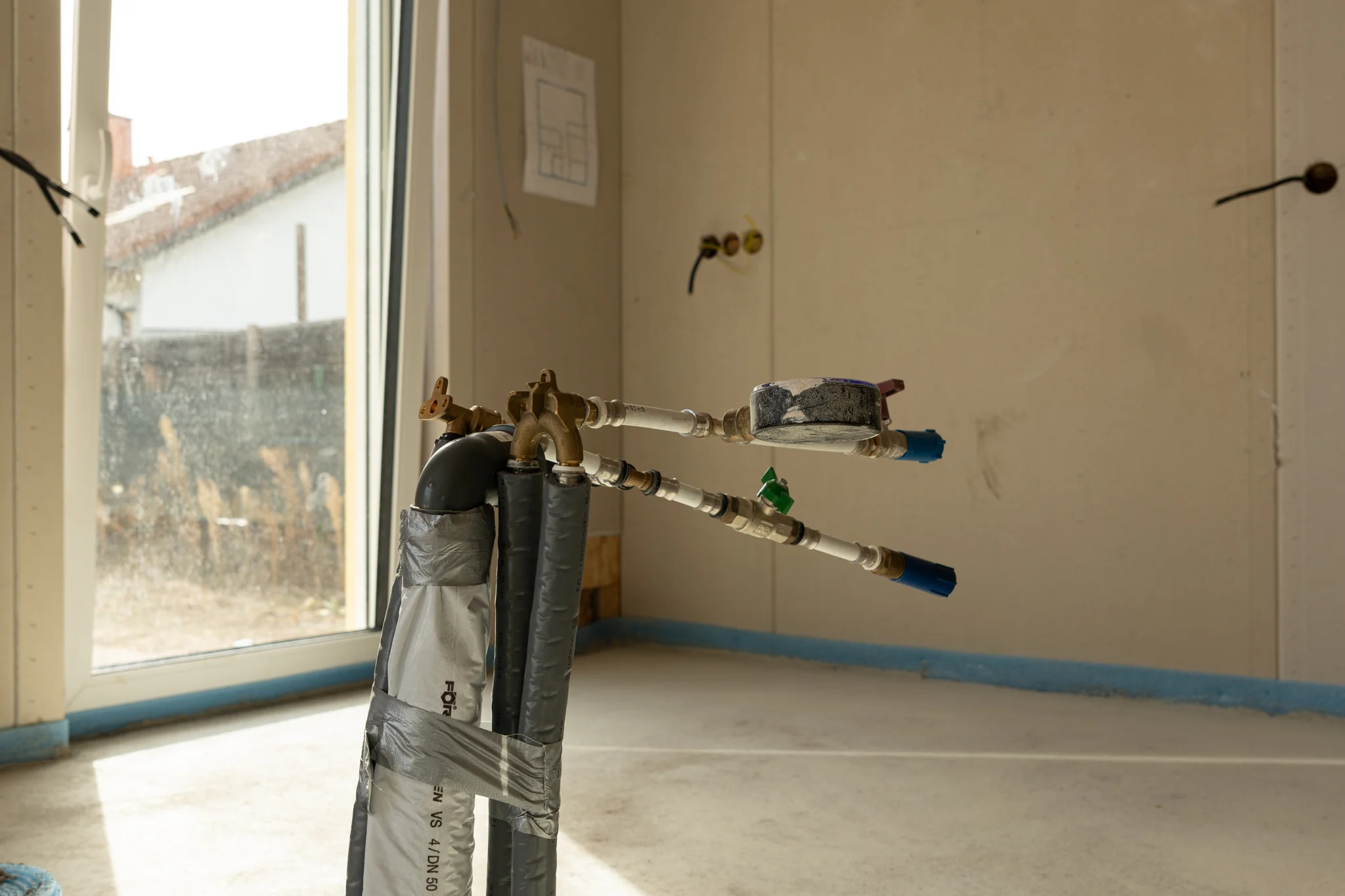 Vorbereitete Rohrleitungen und Armaturen vor einer bodentiefen Fenstertür