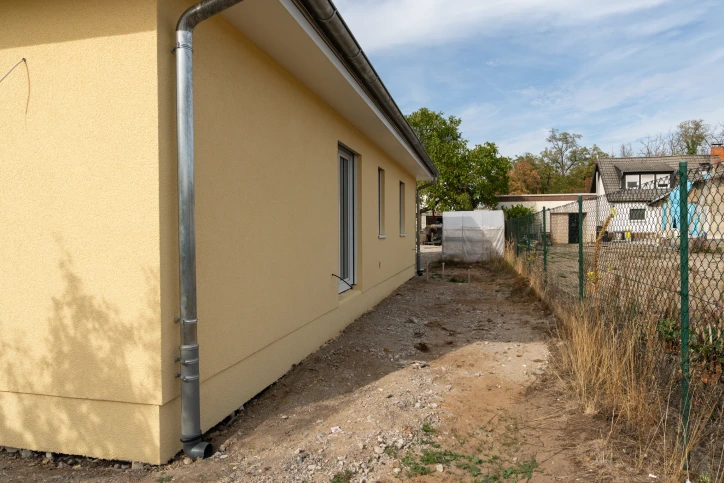 Seitenfassade des Bungalows mit Fenstern und Weg entlang der Grundstücksgrenze