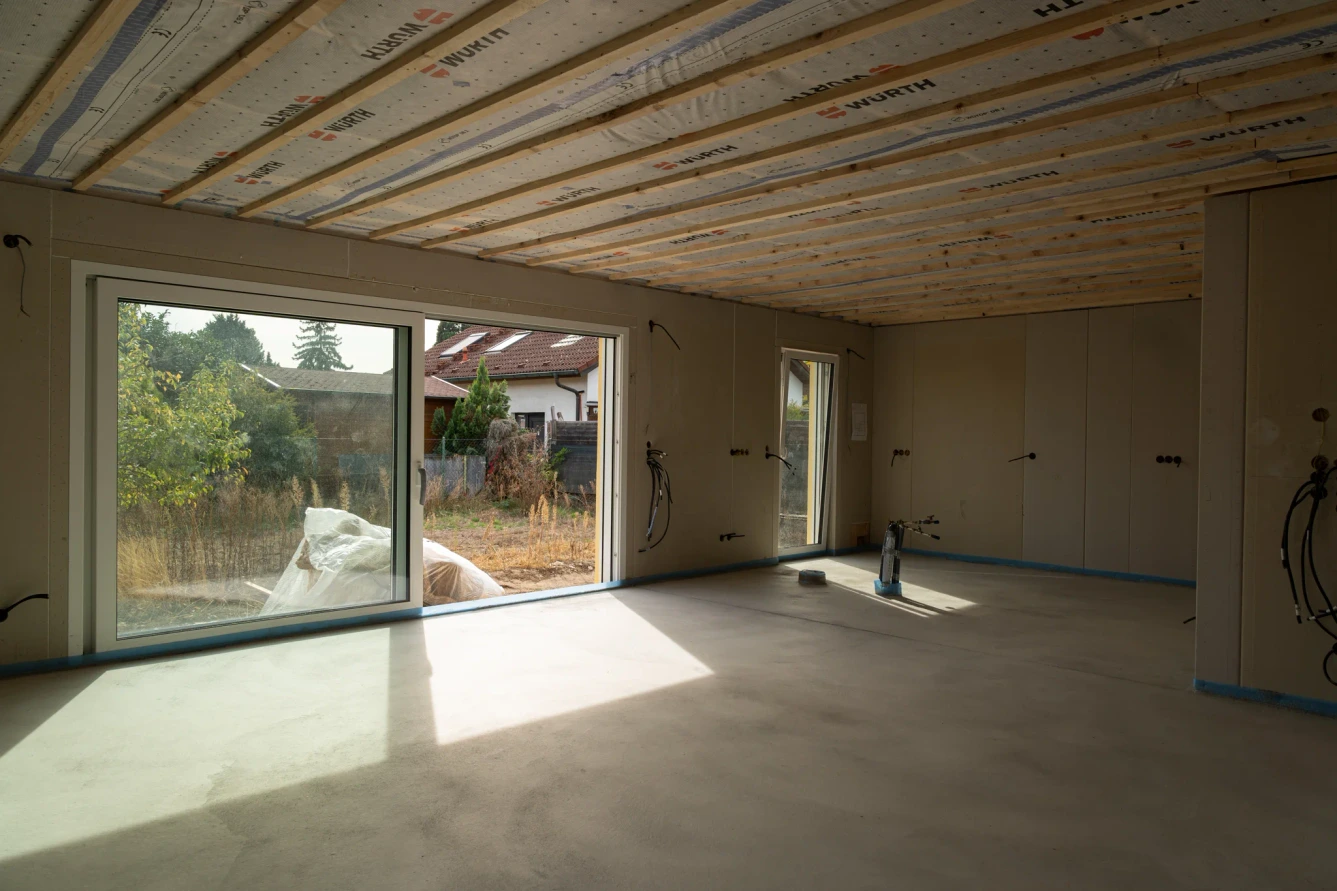 Wohnbereich im Ausbau mit breiter Fensterfront links und sichtbarer Deckenunterkonstruktion