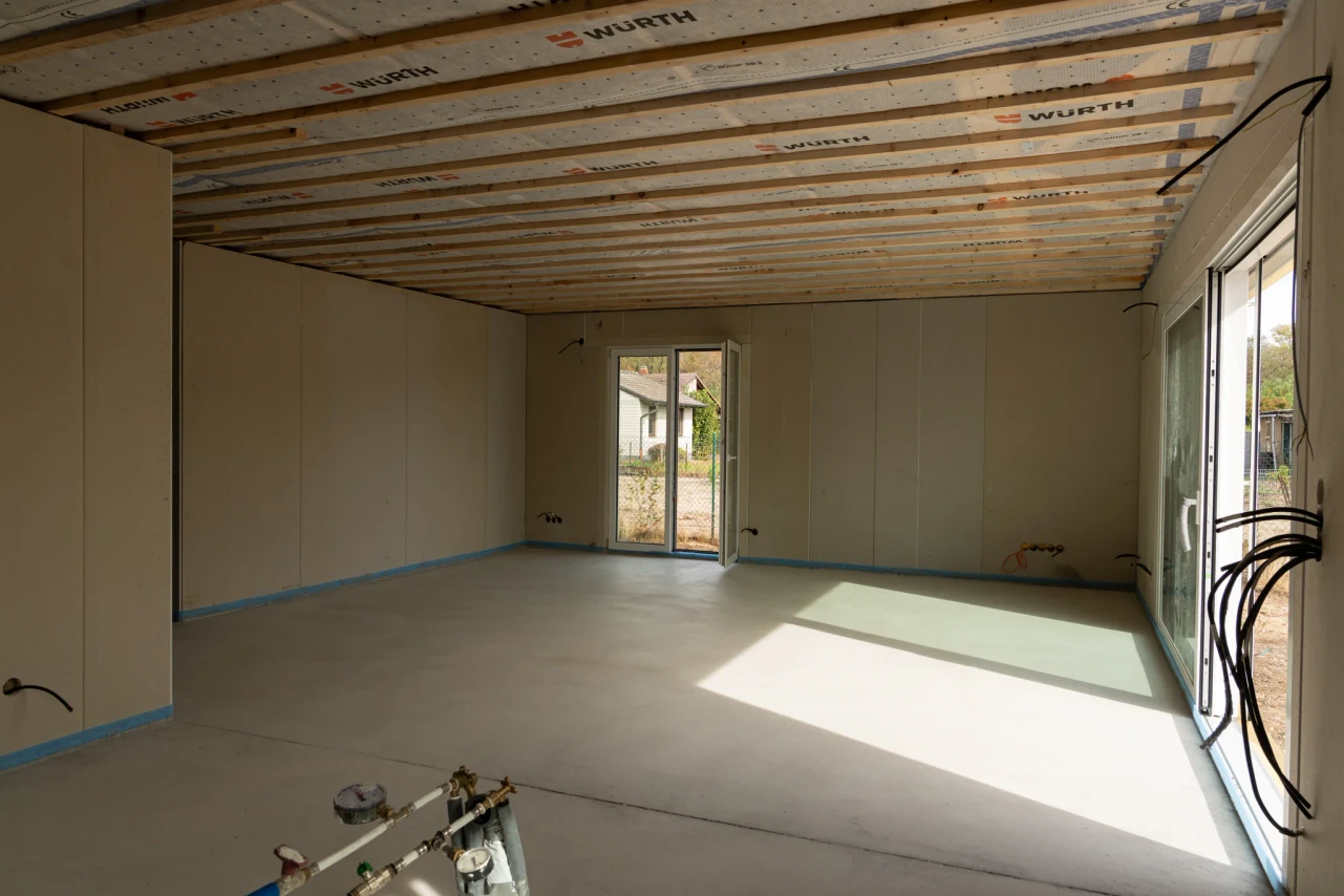 Wohnbereich im Ausbau mit bodentiefen Fenstern und Leitungsanschlüssen im Vordergrund