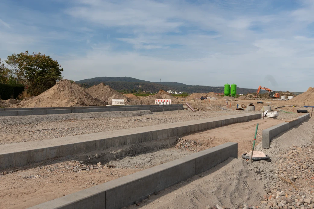 Prepared road surfaces with kerbs, soil heaps and an excavator at the Am Schwabenbach development in Wachenheim